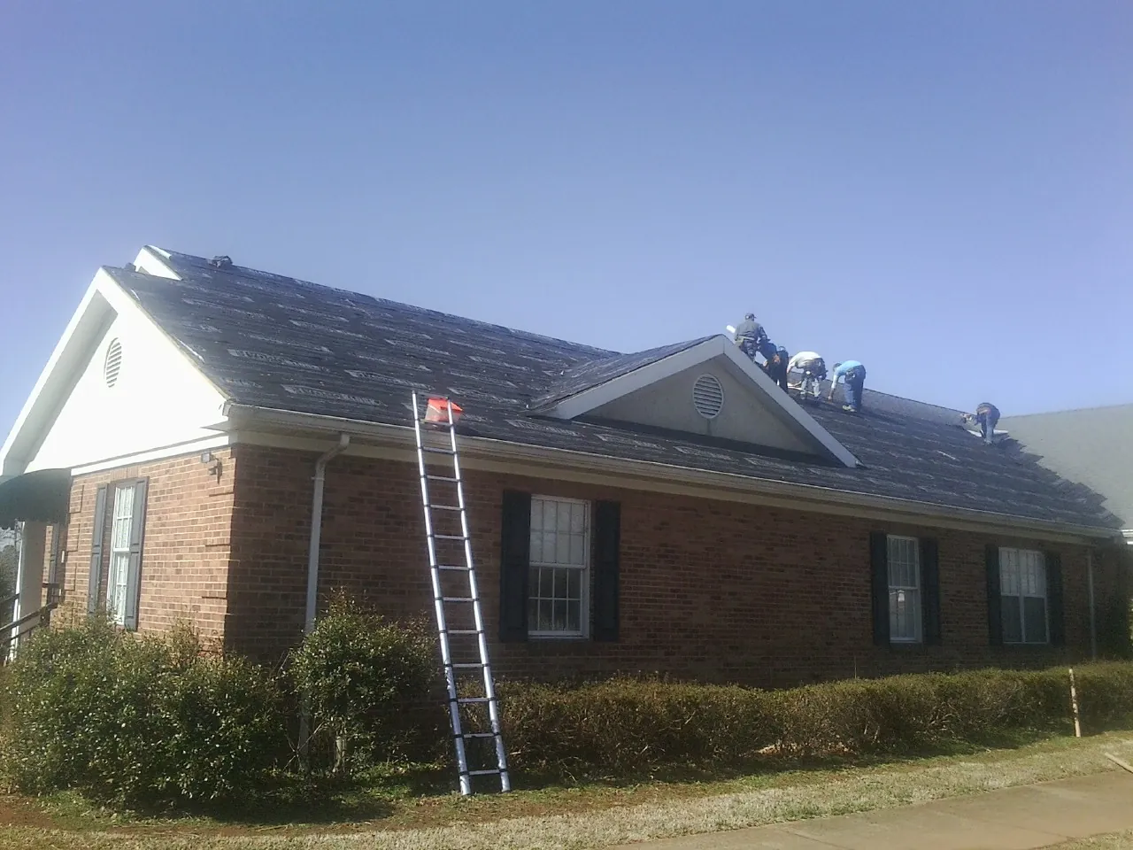 Crew tearing shingles off a brick ranch roof with a ladder set — Metal Roof Repair work by our crew in Clarendon