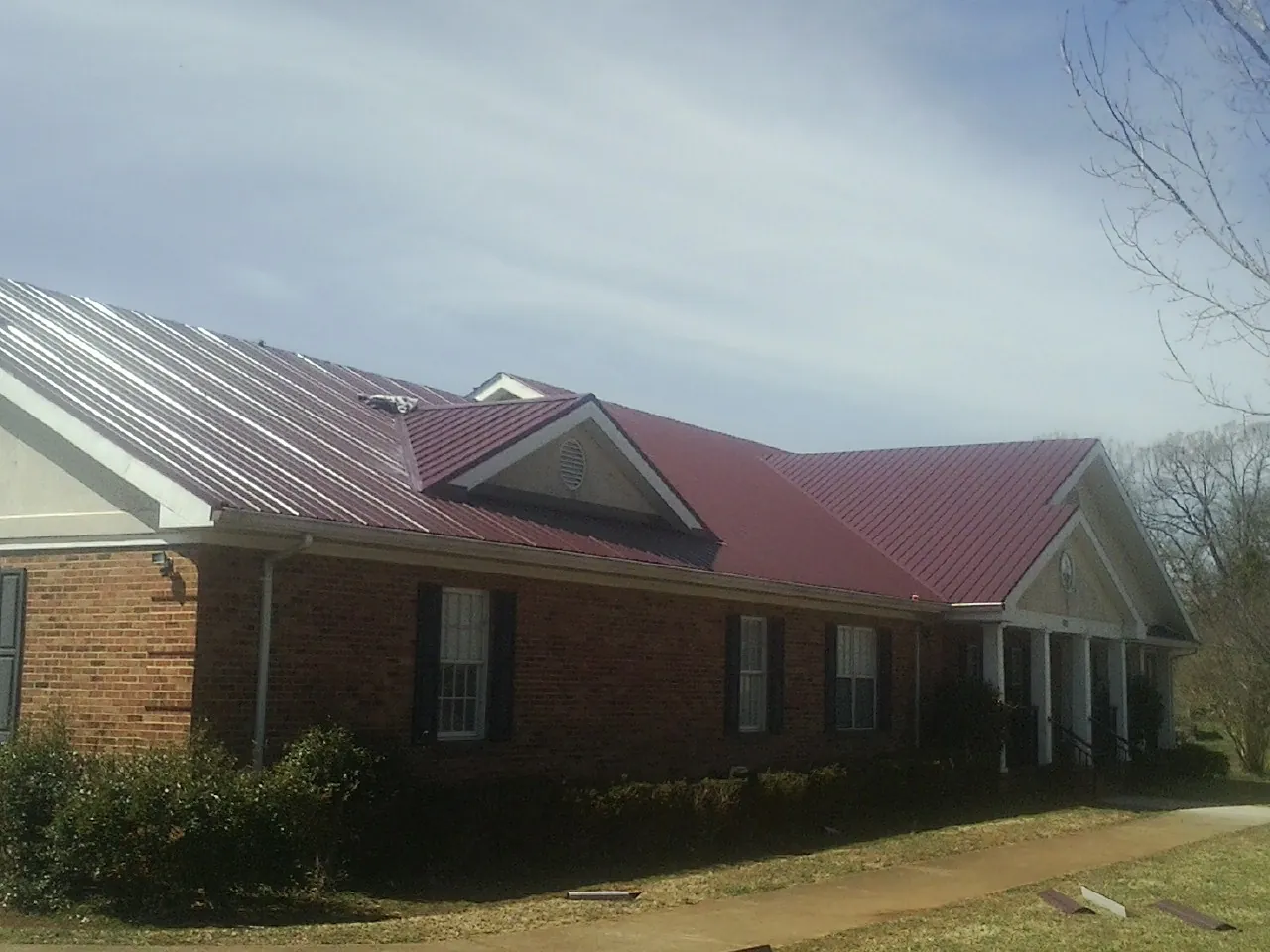 Red metal roof with gabled entries on a long brick building, from a Hail Damage Roof Repair job in Clarendon