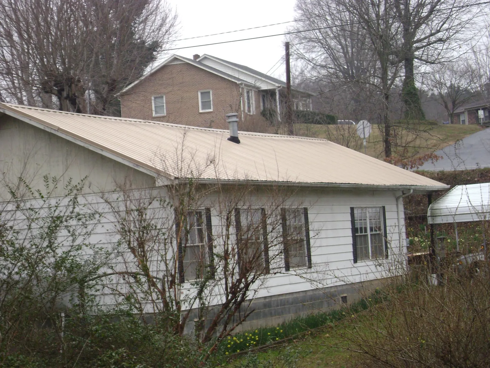 Tan metal roof on a white sided house set into a hillside — Commercial Roofing by Roofing Brothers in Clarendon